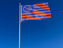 Load image into Gallery viewer, 3x5 foot wide USA Flag style Boise State University Flag with blue &amp; orange stripes and two metal grommets attached to flagpole waving in the wind
