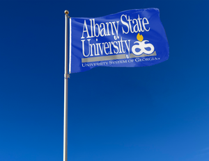 Blue 3x5 foot wide Albany State University Flag with University System of Georgia Logo and two metal grommets attached to a flagpole as it waves in the wind