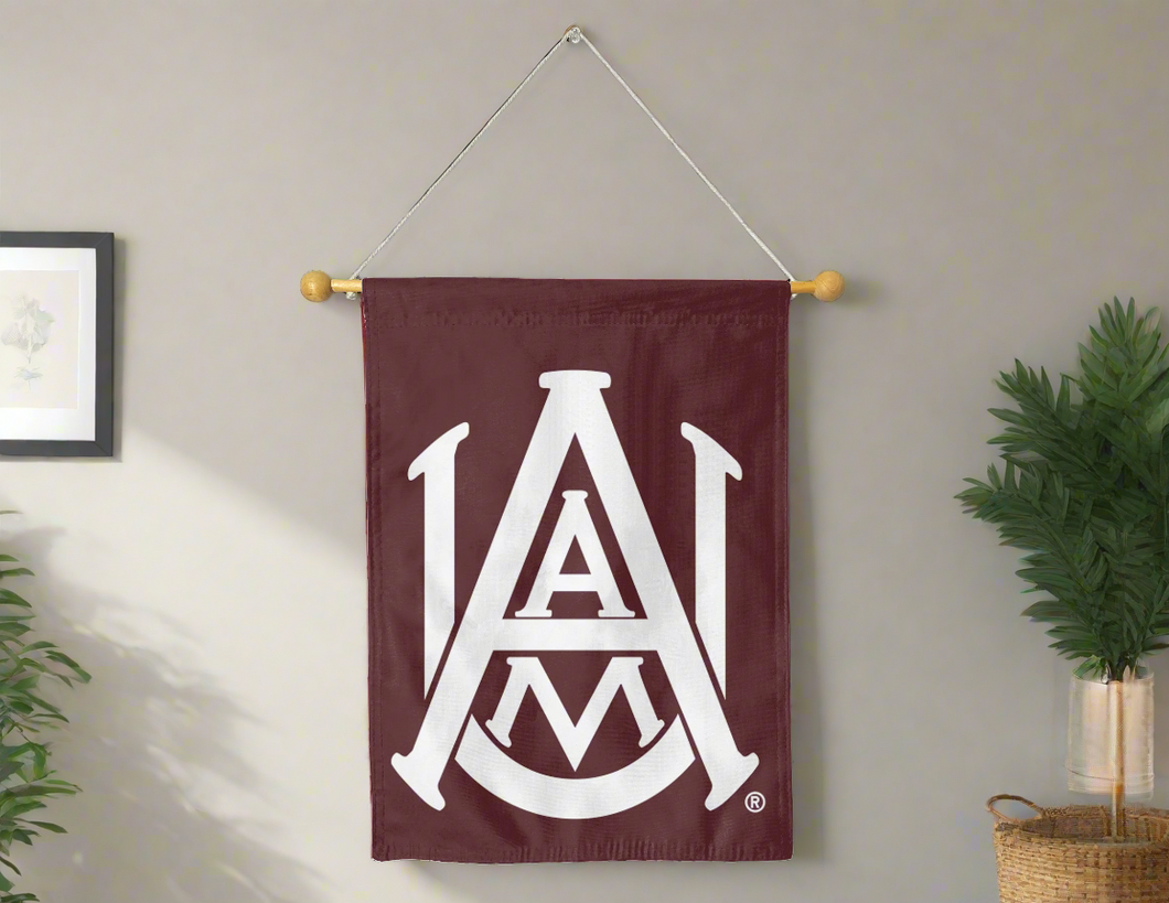 30x40 inch long Alabama A&M University House Flag hung on a banner pole in front of a grey wall with one plant on the left side and another one on the right side