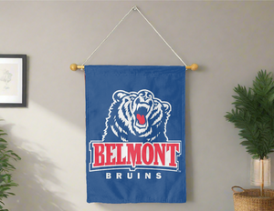 Blue 30x40 inch long Belmont University House Flag hung on banner pole inside a room with one plant on the right and left side