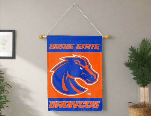 30x40 inch long 3 Panel Blue Orange Blue Boise State University House Flag with Broncos Logo hung on a banner pole inside a room with gray wall and one plant on the right and left sides