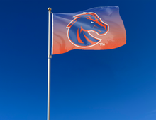 Load image into Gallery viewer, Gradient Orange to Blue 3x5 Foot wide Boise State University Flag with two metal grommets attached to flagpole waving in the wind
